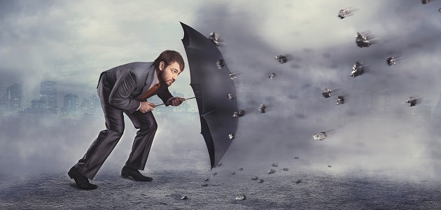 Business man protects himself from rocks with umbrella over grey